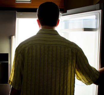 Man looking for food in an open fridge in a dark kitchen late at night