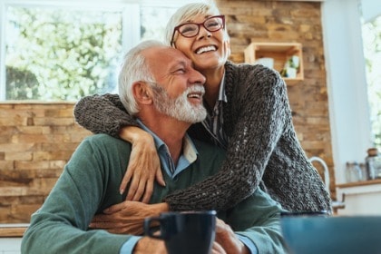 mature-couple-hugging-at-kitchen-table-happy-laughing